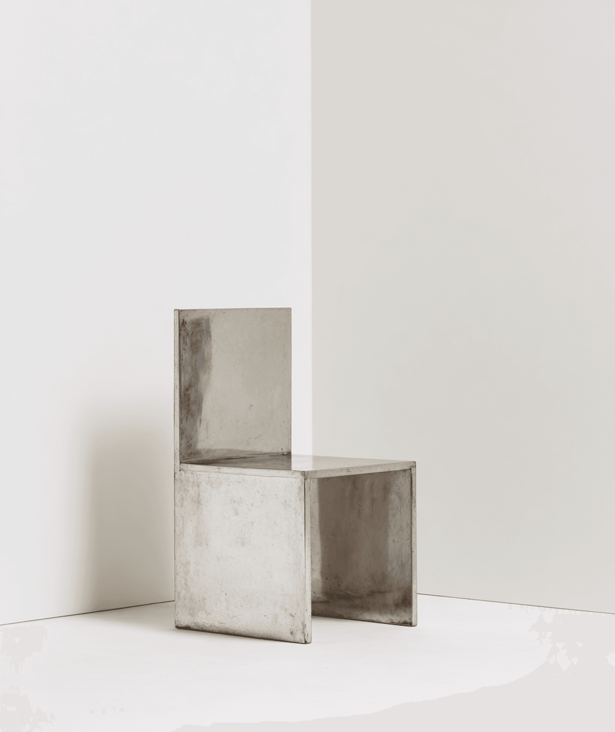 Minimalist brushed-steel chair in a white corner studio—industrial, brutalist modern furniture.